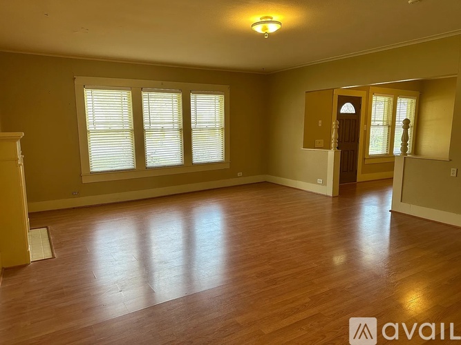A spacious room with wooden floors and a large window with white blinds.
