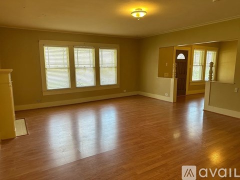 A spacious room with wooden floors and a large window with white blinds.