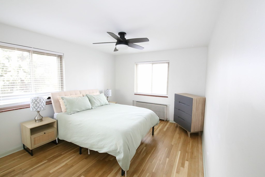 A bedroom with a bed, nightstand, and a fan.
