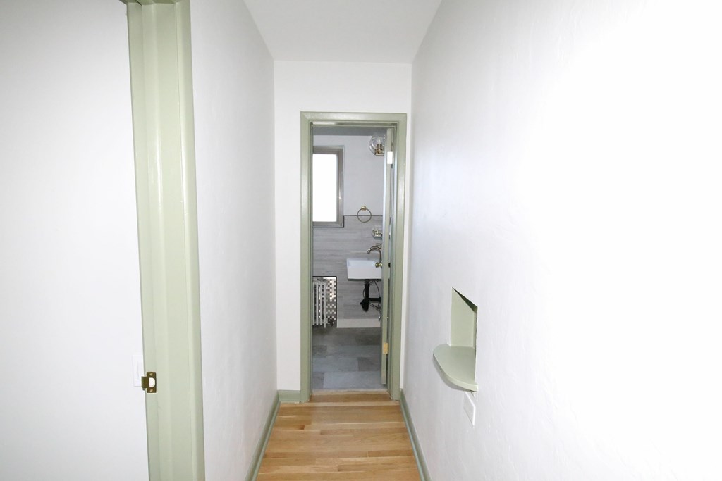 A hallway with a door on the left and a mirror on the right.