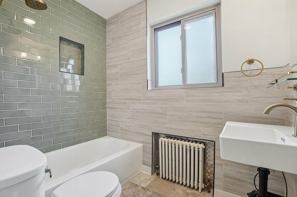 A bathroom with a white toilet, a white sink, a white bathtub, and a window.