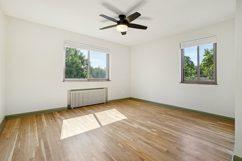 A room with a ceiling fan and two windows.