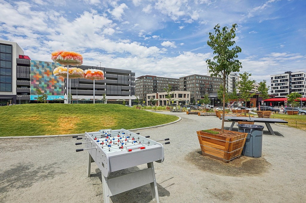 A table with a foosball game on it is in the foreground of a park with a building in the background.