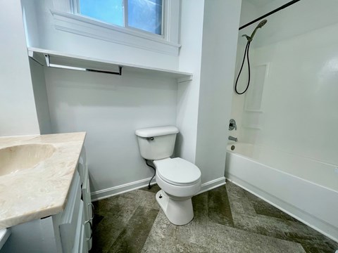 A white toilet sits in a bathroom next to a sink and a bathtub.