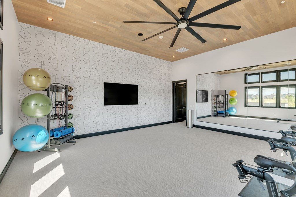 A spacious room with a ceiling fan, exercise equipment, and a television.
