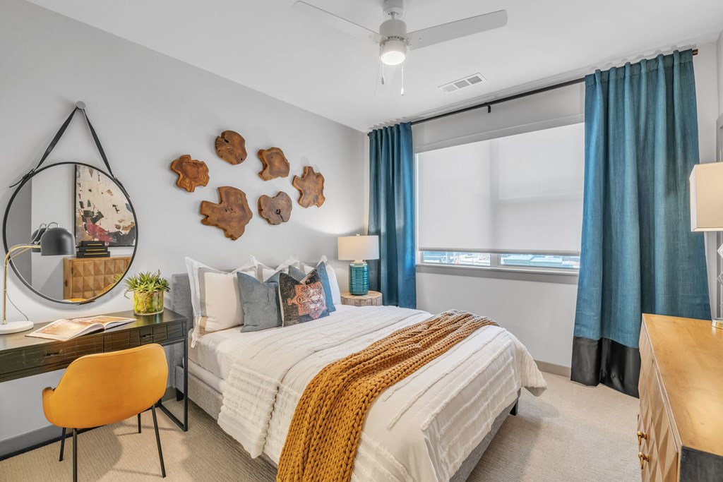 A bedroom with a bed, desk, chair, and a mirror.