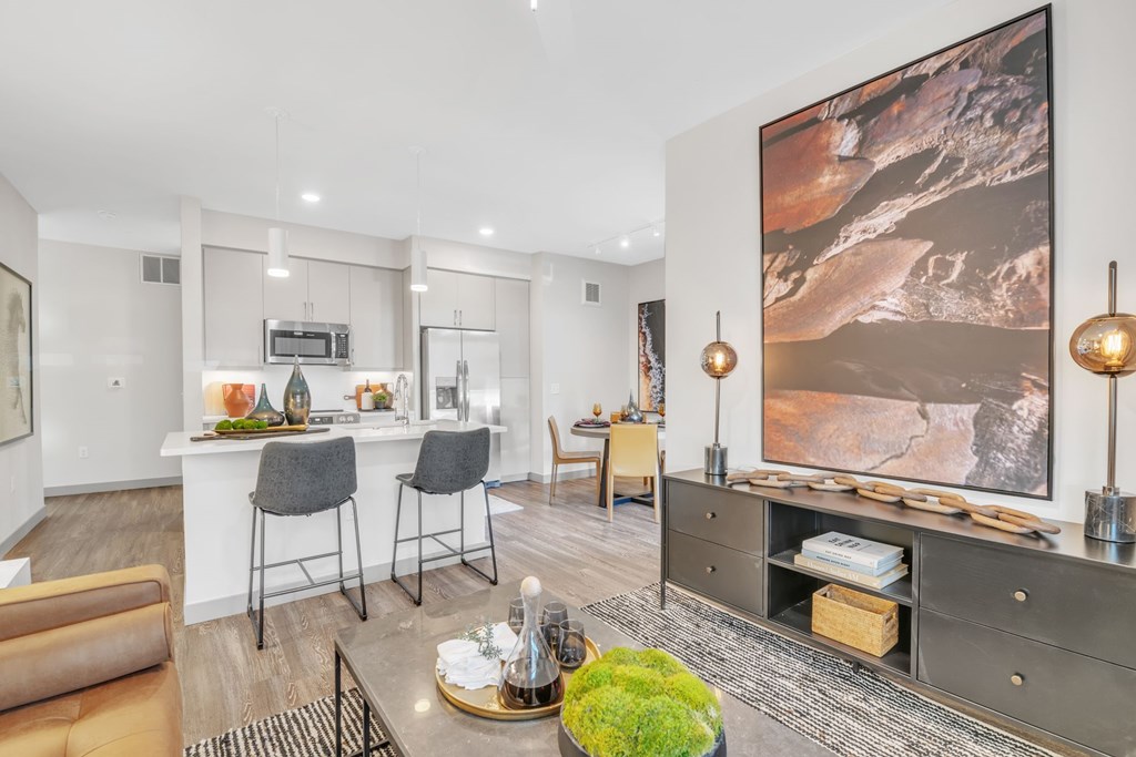 A modern living room with a large painting on the wall and a dining area with chairs and a table.