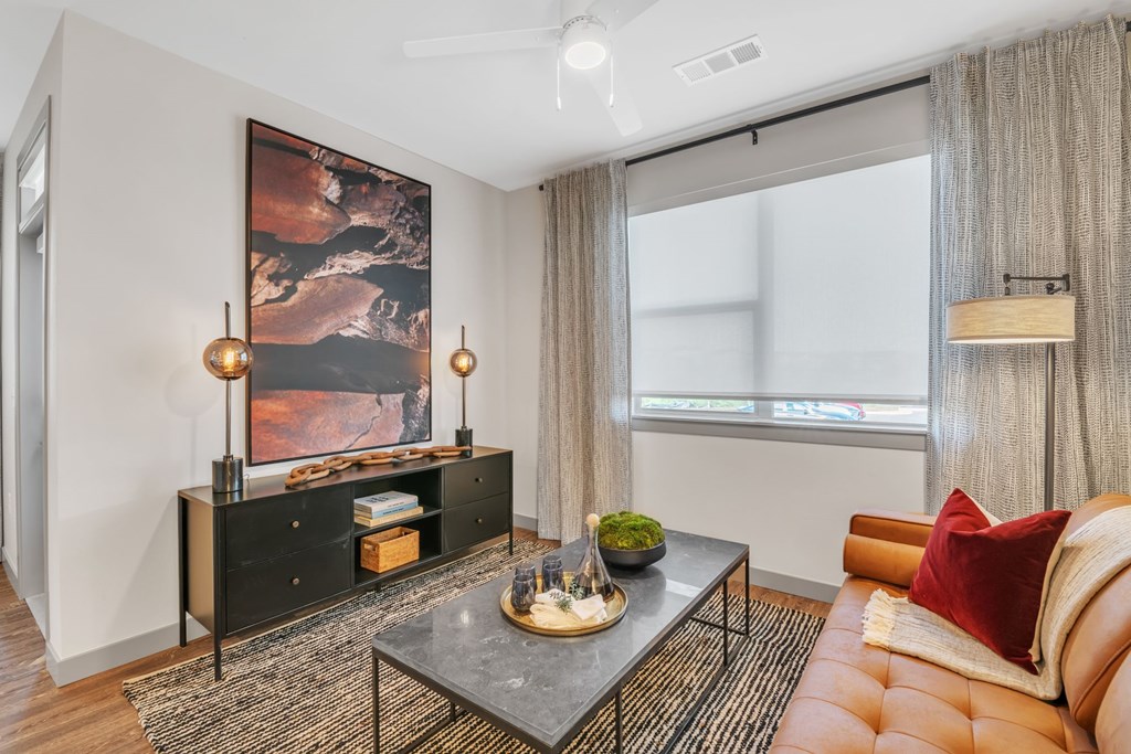 A living room with a brown leather couch, a black coffee table, and a large painting on the wall.