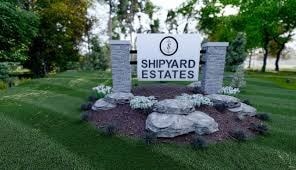 A sign for Shipyard Estates is surrounded by rocks and flowers.