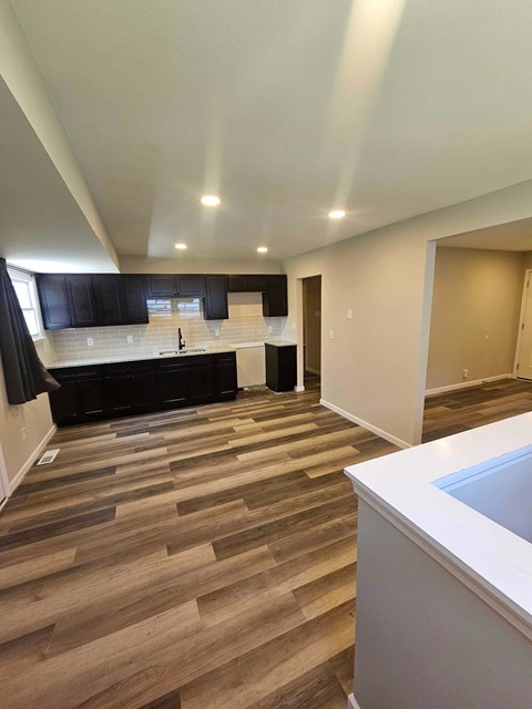 A kitchen with a white counter top and wooden flooring.