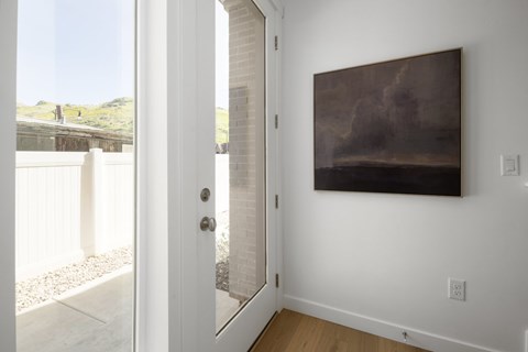 A painting hangs on a white wall in a room with a white door.