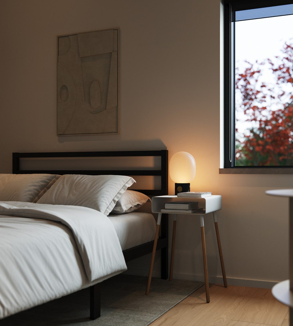 A bedroom with a bed, a table with a lamp, and a framed picture on the wall.