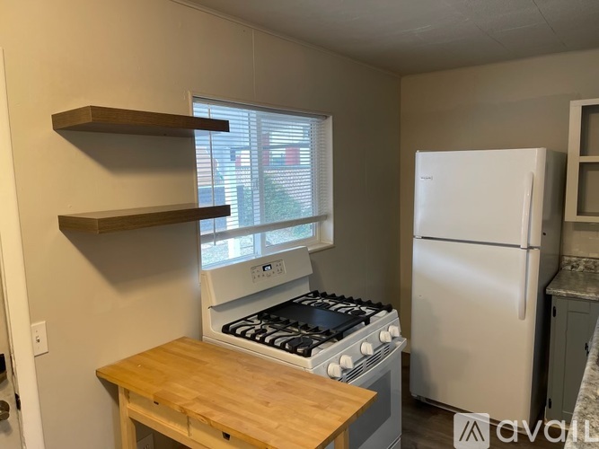 A kitchen with a white refrigerator, a wooden table, and a stove with a window above it.