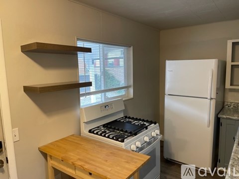 A kitchen with a white refrigerator, a wooden table, and a stove with a window above it.