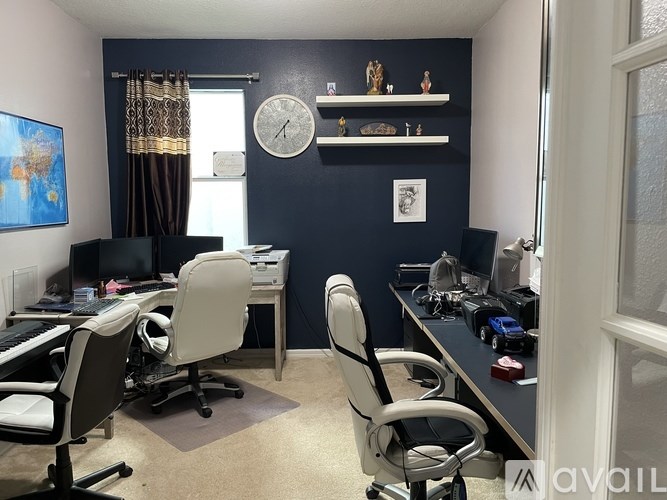 A room with a desk and chairs, a computer, and a clock on the wall.