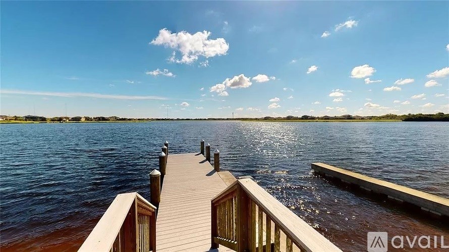 A wooden dock extends into a calm body of water under a clear blue sky.