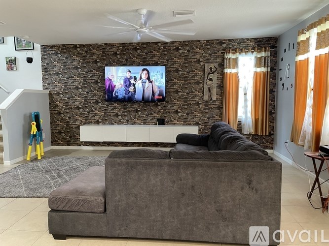 A living room with a grey couch and a stone wall with a television mounted on it.