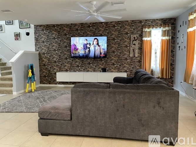 A living room with a grey couch and a television on a stone wall.