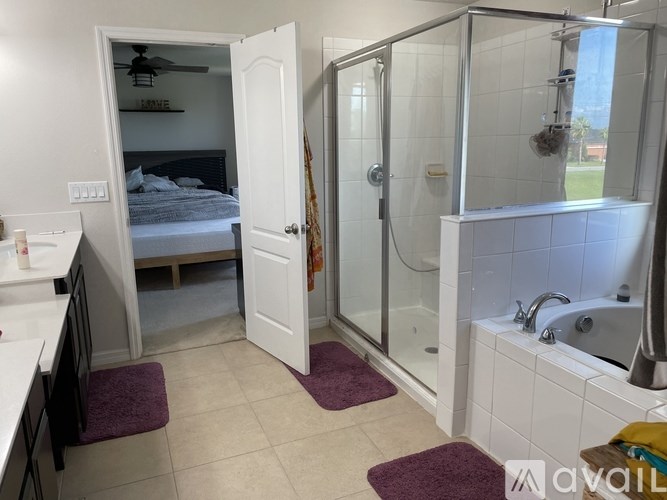 A bathroom with a walk-in shower and a bedroom with a bed and a ceiling fan.
