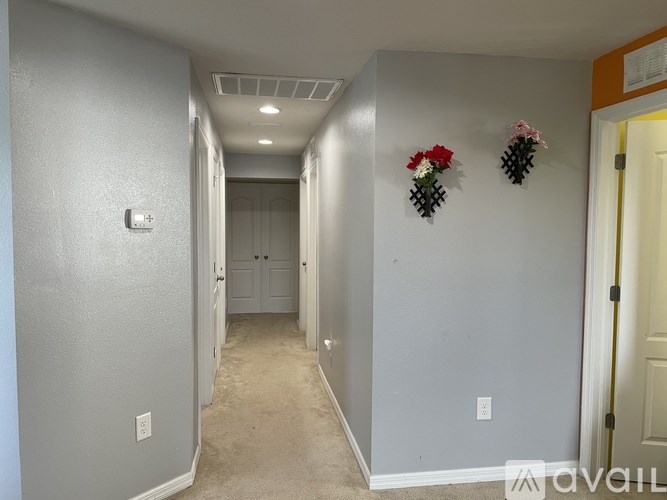 A hallway with two doors at the end and two flower arrangements on the wall.