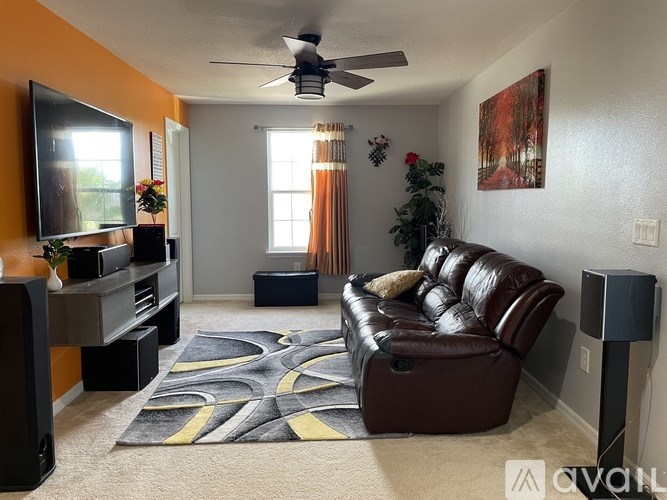 A living room with a brown leather couch and a ceiling fan.