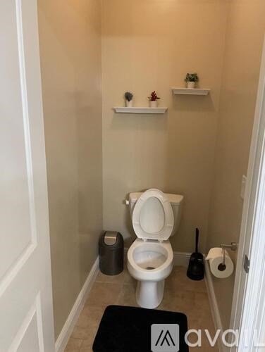 A bathroom with a toilet, a trash can, and a black mat on the floor.