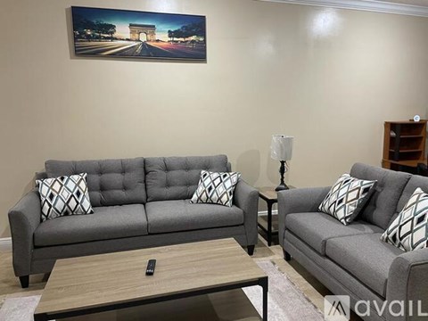 A living room with a grey couch, a coffee table, and a painting of the Eiffel Tower on the wall.