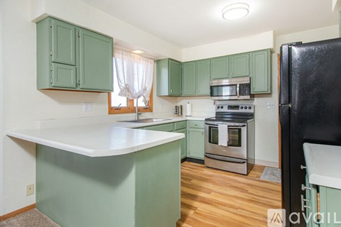 A kitchen with green cabinets and a black refrigerator.