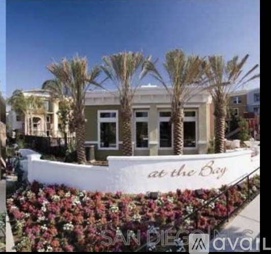 A white boat with the words "at the Bay" written on it is in front of a building with palm trees.