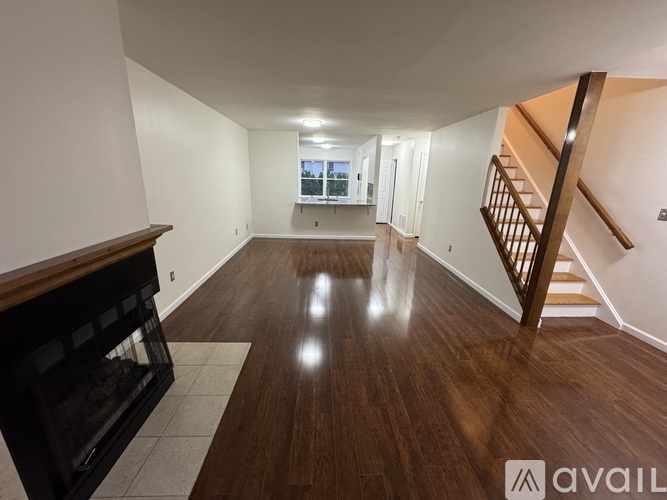 A spacious room with wooden floors and a staircase on the right side.
