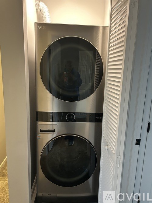 A stainless steel front loading washing machine with a black door is in a room.