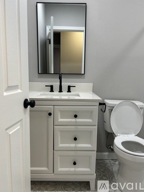 A bathroom with a white toilet and a white sink with a cabinet and a mirror above it.