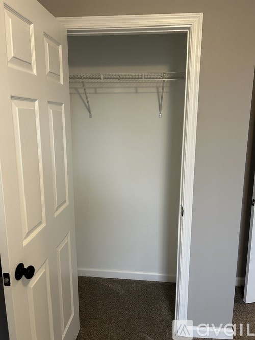 A white door with a black handle is open to a white closet with a shelf and hangers.