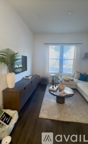 A living room with a white couch, a wooden cabinet, and a flat-screen TV mounted on the wall.