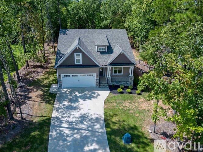 A house with a garage is surrounded by trees and has a driveway leading to the front door.