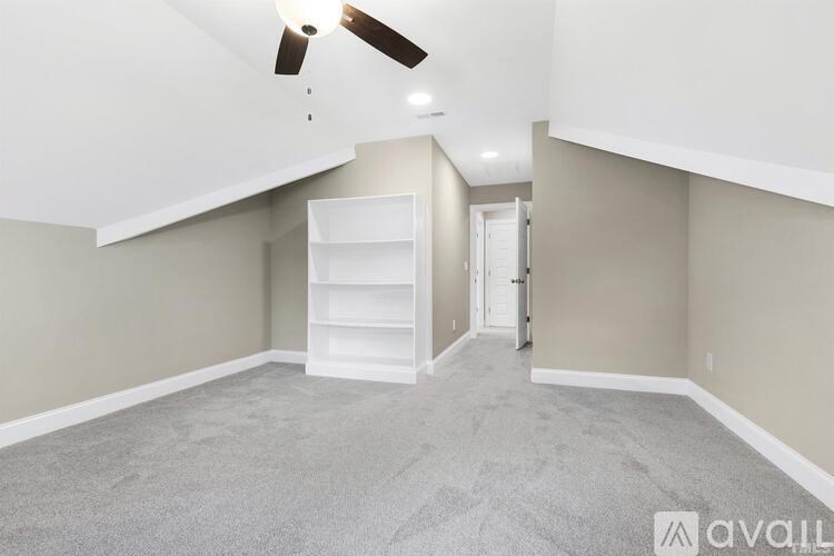 A spacious room with a ceiling fan and a white bookshelf.