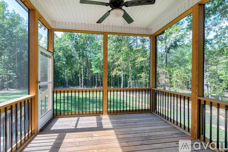 A wooden deck with a ceiling fan and glass walls overlooking a grassy area.