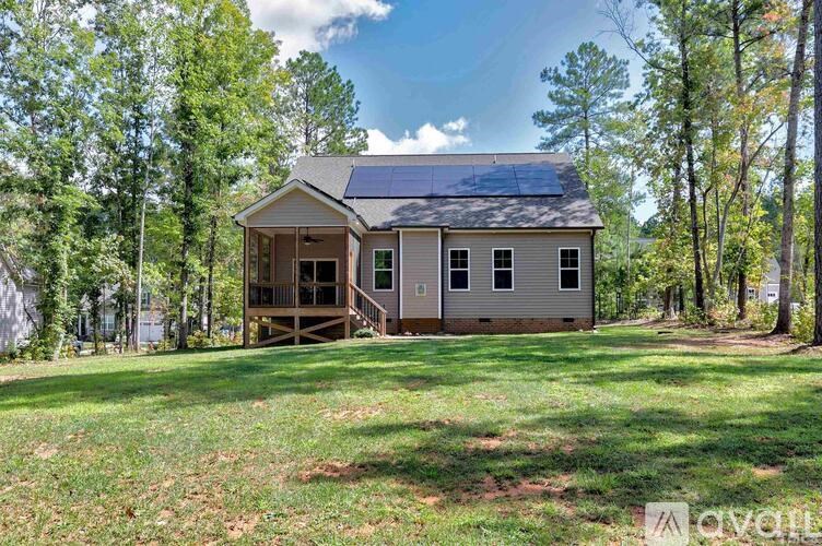 A house with a solar panel on the roof is surrounded by trees and grass.
