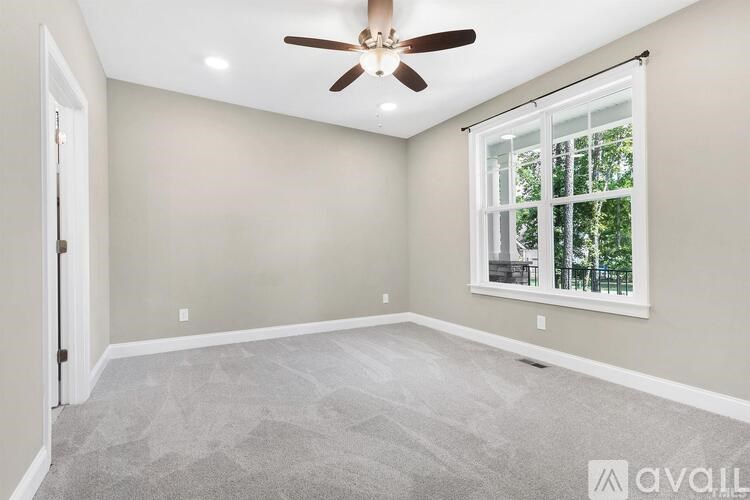 A room with a ceiling fan and a window with a view of trees.