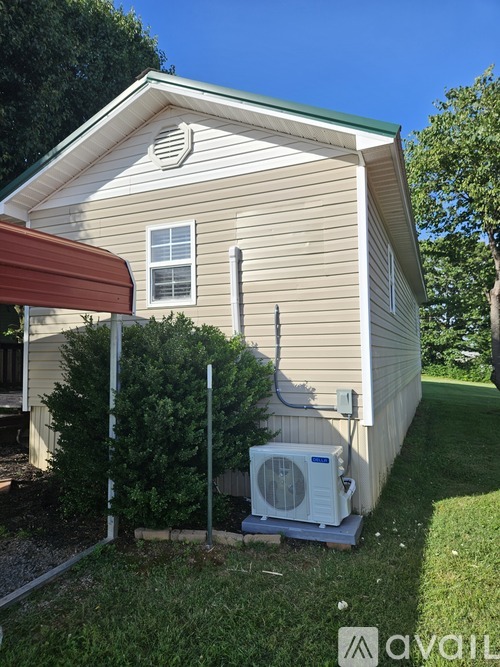 A house with a tan siding and a red awning with a window and a fan on the ground.