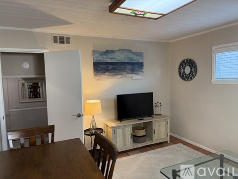 A living room with a wooden table and chairs, a television, and a painting of a beach scene on the wall.