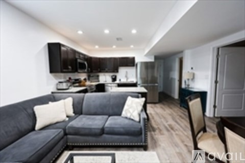A modern living room with a black couch and a kitchen area in the background.