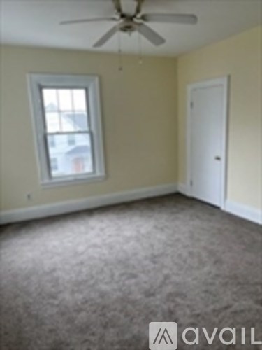A room with a carpeted floor, a ceiling fan, and a window.