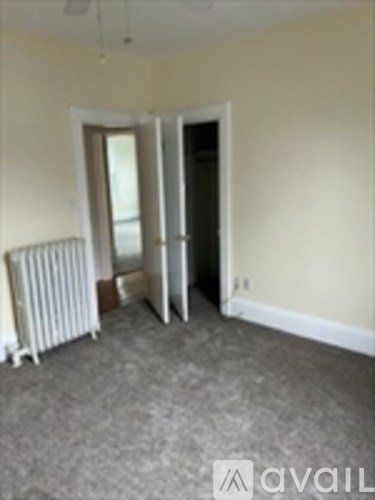 A room with a carpeted floor, a white radiator, and a white door.