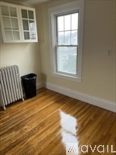 A room with a window and a radiator with a trash can.