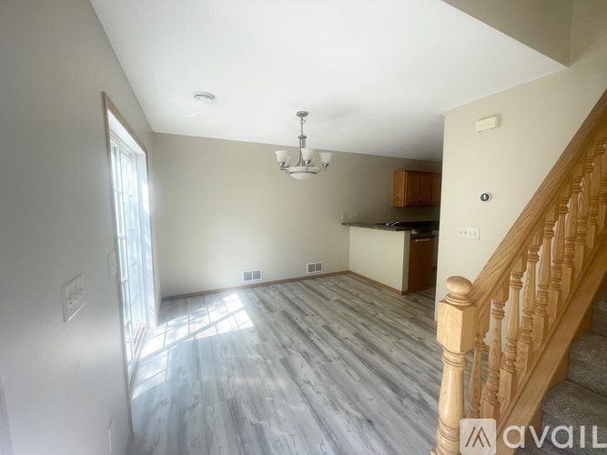 A spacious living room with wooden flooring and a staircase on the right side.