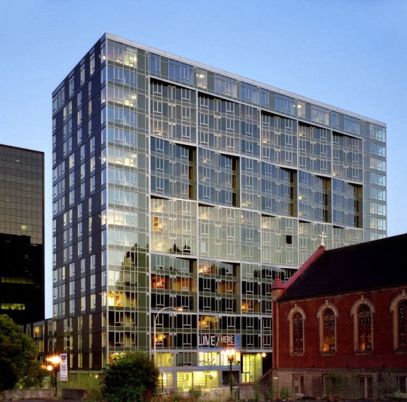 a tall building with a glass facade and a city at dusk