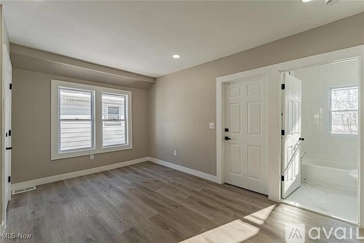 A room with a white door, a window with blinds, and a wooden floor.