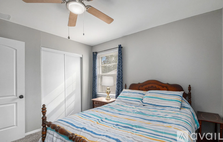 A bedroom with a bed, a ceiling fan, and a window with curtains.