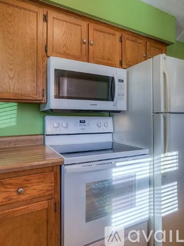 A kitchen with a white stove and refrigerator, wooden cabinets, and a green wall.
